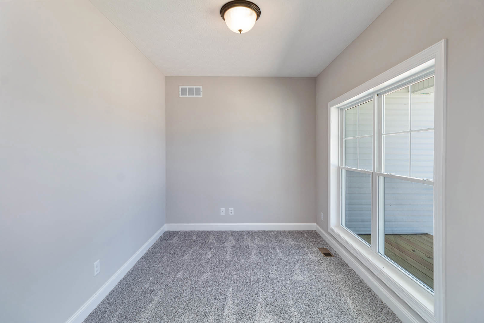 Carpeted room with patterned flooring, white plaster walls, ceiling light fixture, window with daylight, wall vent, and decorative molding