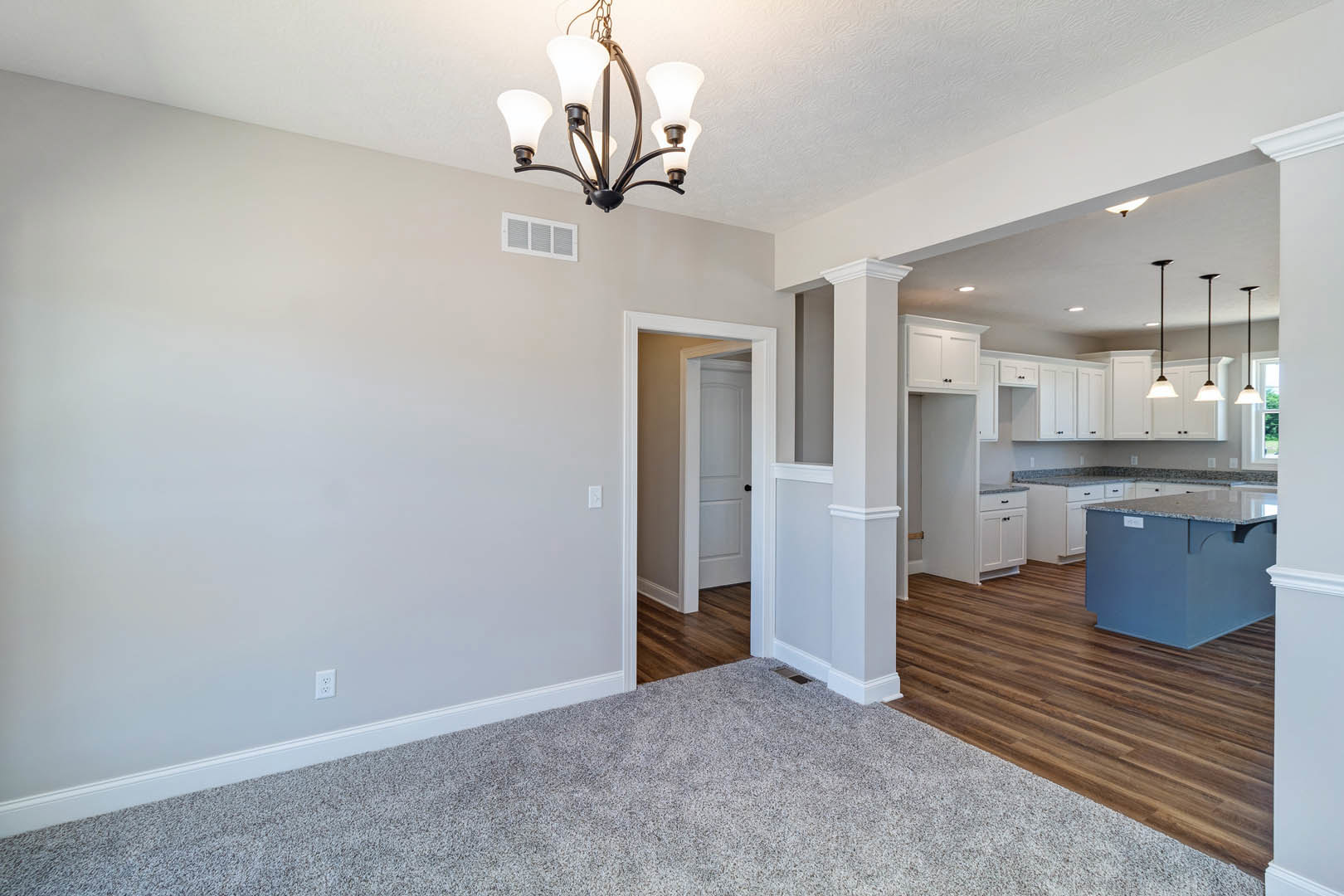 Open kitchen with marble-topped island, wood cabinetry, stainless sink, hardwood flooring, white area rug, and decorative chandelier under plaster ceiling