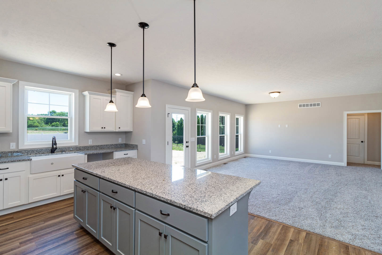 Spacious kitchen featuring a large granite island, tile flooring, white cabinetry, stainless steel sink, and a window overlooking a grassy field