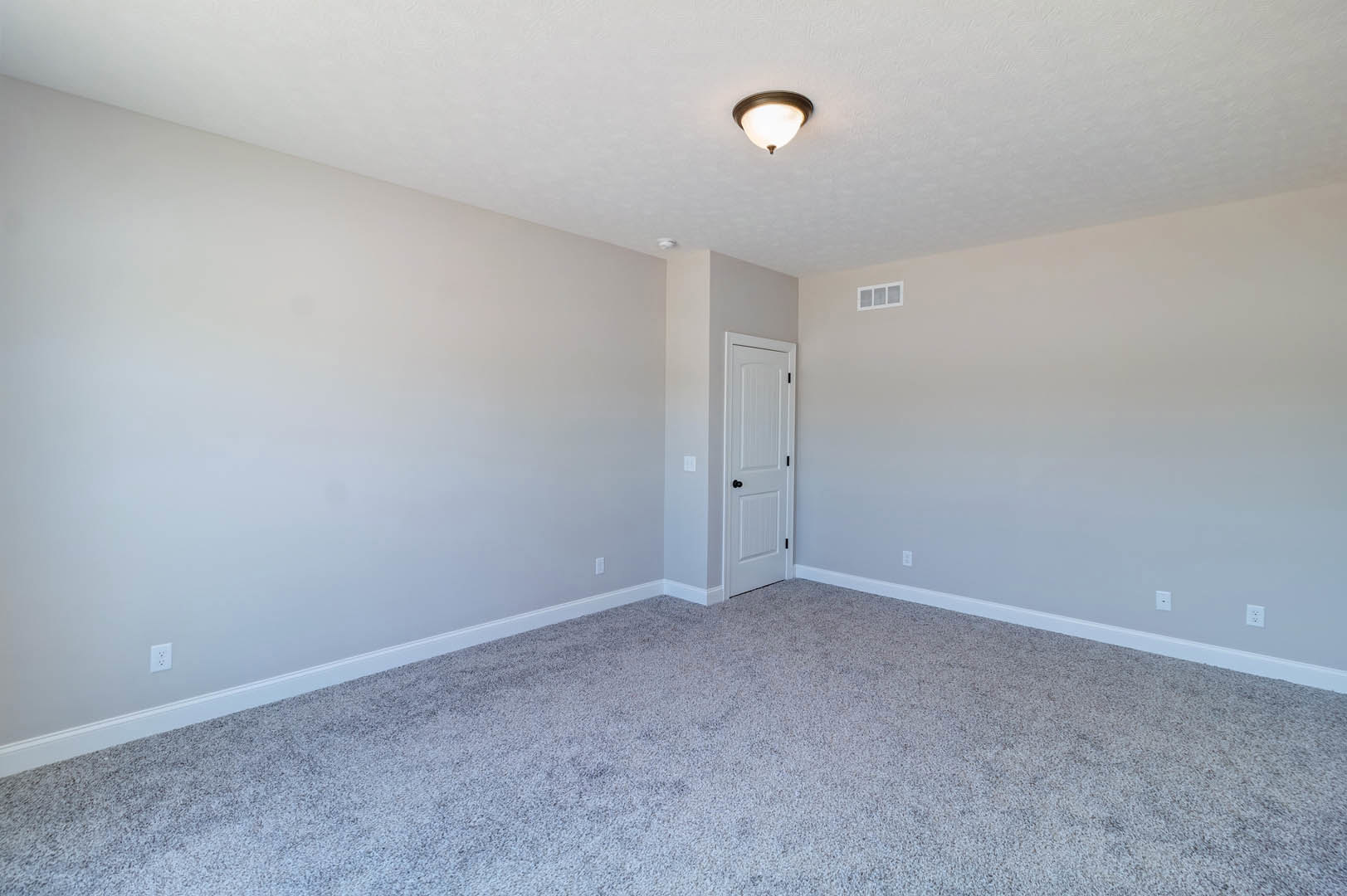 White walls and plush beige carpet in a room with a white door featuring black knobs, round ceiling light fixture, and simple trim.