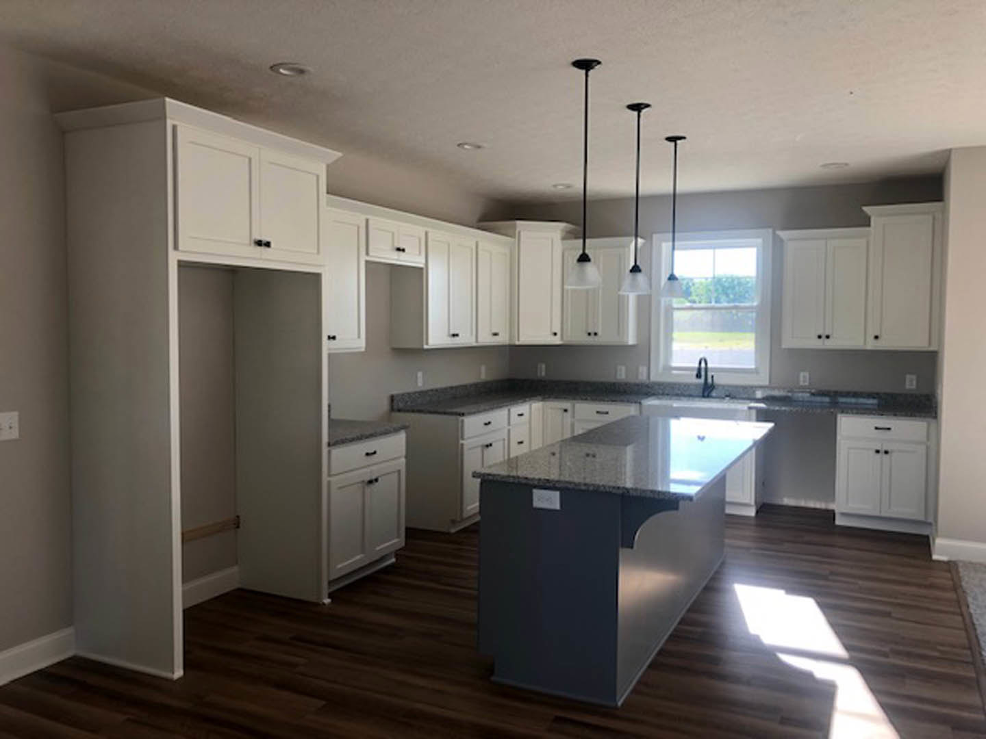 White cabinetry and black countertops in a kitchen with a marble-topped island, stainless steel sink, pendant light fixture near a window, and a white-framed closet door