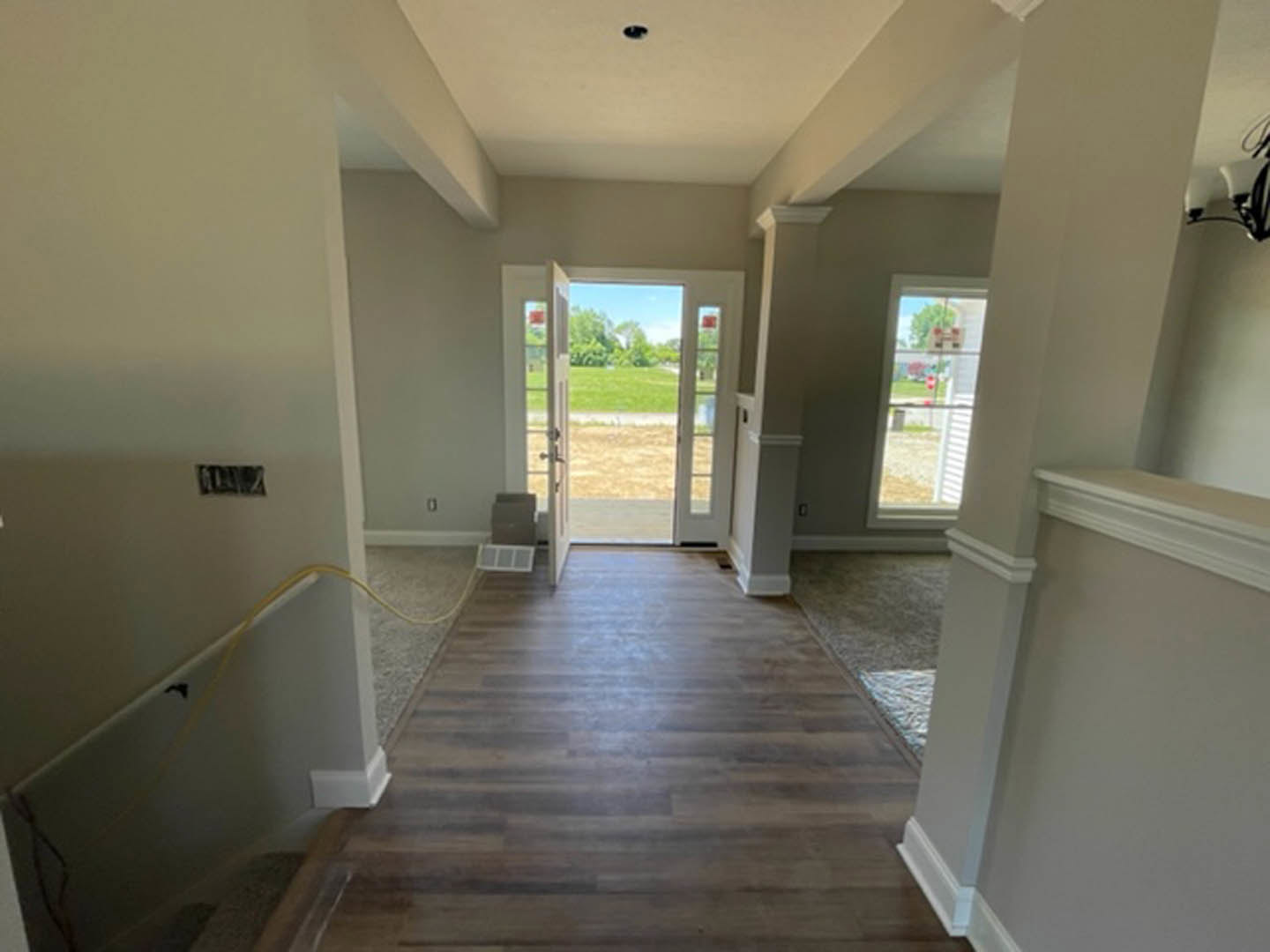 Hallway with hardwood flooring, white plaster walls, wooden door at the end, molding trim, and window overlooking grassy field