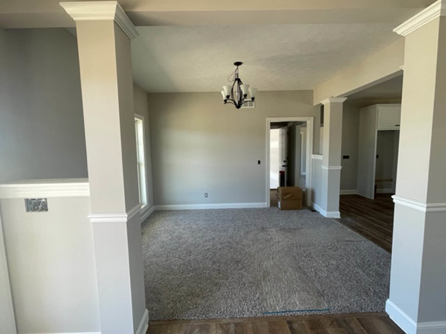 Neutral-toned carpeted room with white walls, ceiling molding, and a modern chandelier hanging from the ceiling
