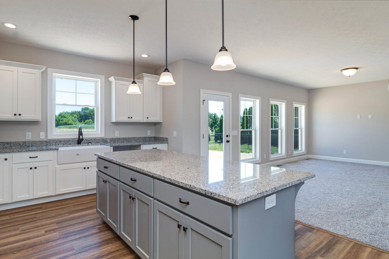Spacious kitchen featuring a large central island with drawers and doors, white tile backsplash, window above the sink overlooking trees, pendant lights hanging from the ceiling