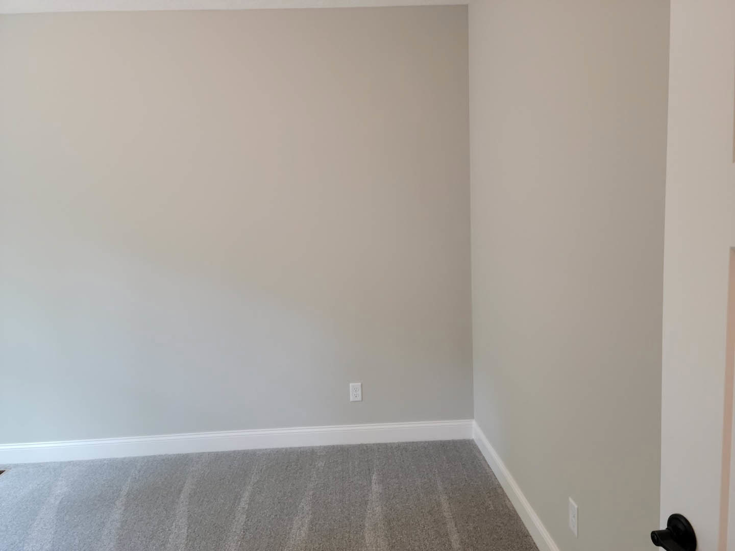 White carpeted floor, smooth white wall with black trim, modern door handle, minimal decor