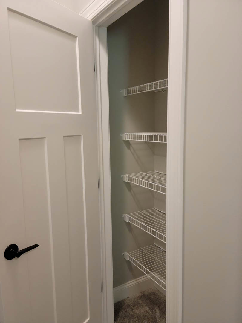 White wire shelves installed in a closet with carpet flooring, white walls, and a close-up view of a silver door handle on a white door.