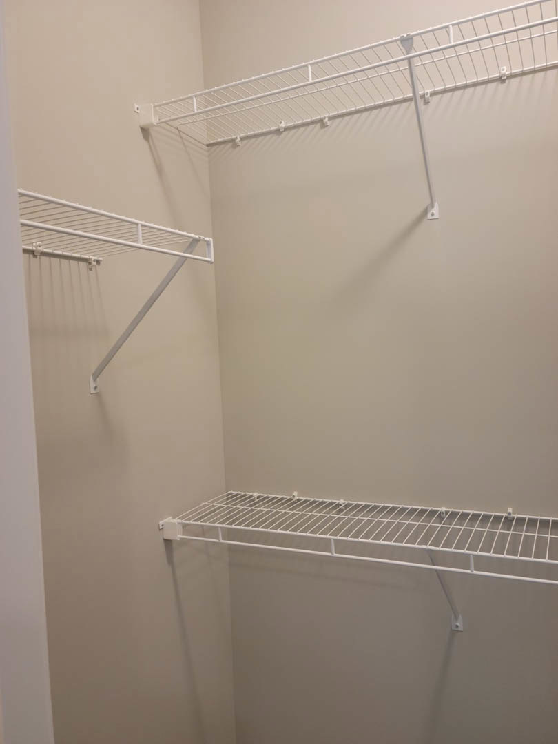 White wire shelf mounted on a grey wall in a room, featuring a metal rod and railing.
