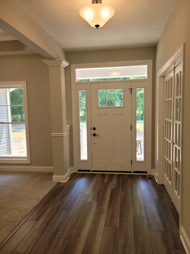 White paneled door with glass inserts, wood laminate flooring, white walls, window with white shutters, and modern light fixture