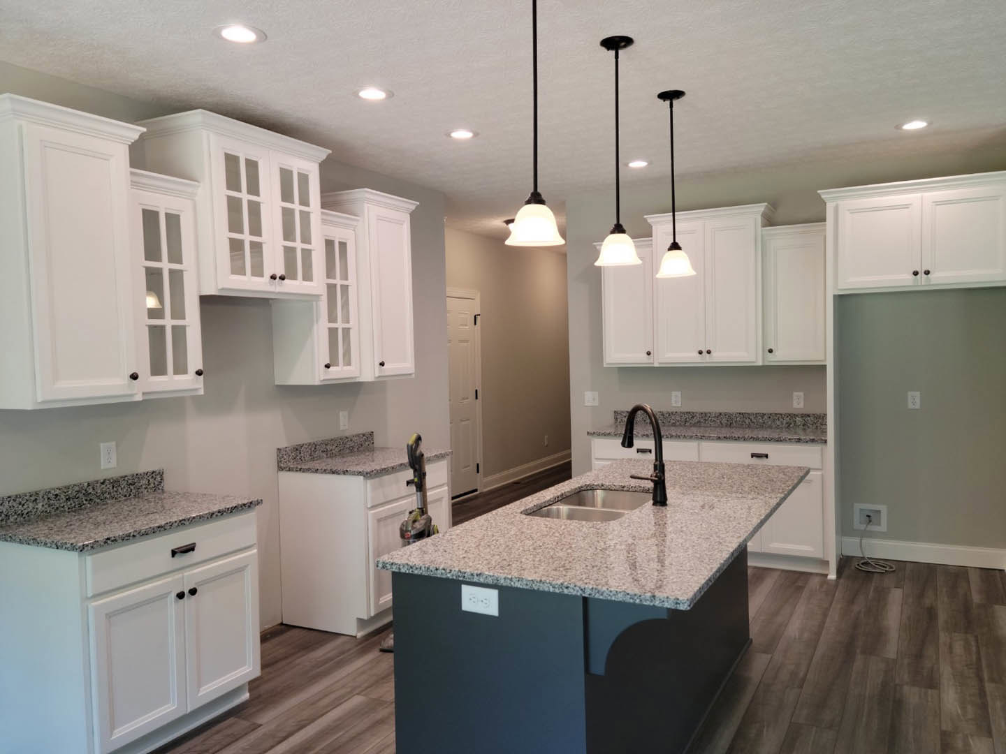 White kitchen cabinets and granite countertops with a central island featuring an undermount sink, stainless faucet, tile backsplash, pendant lighting, and built-in appliances.