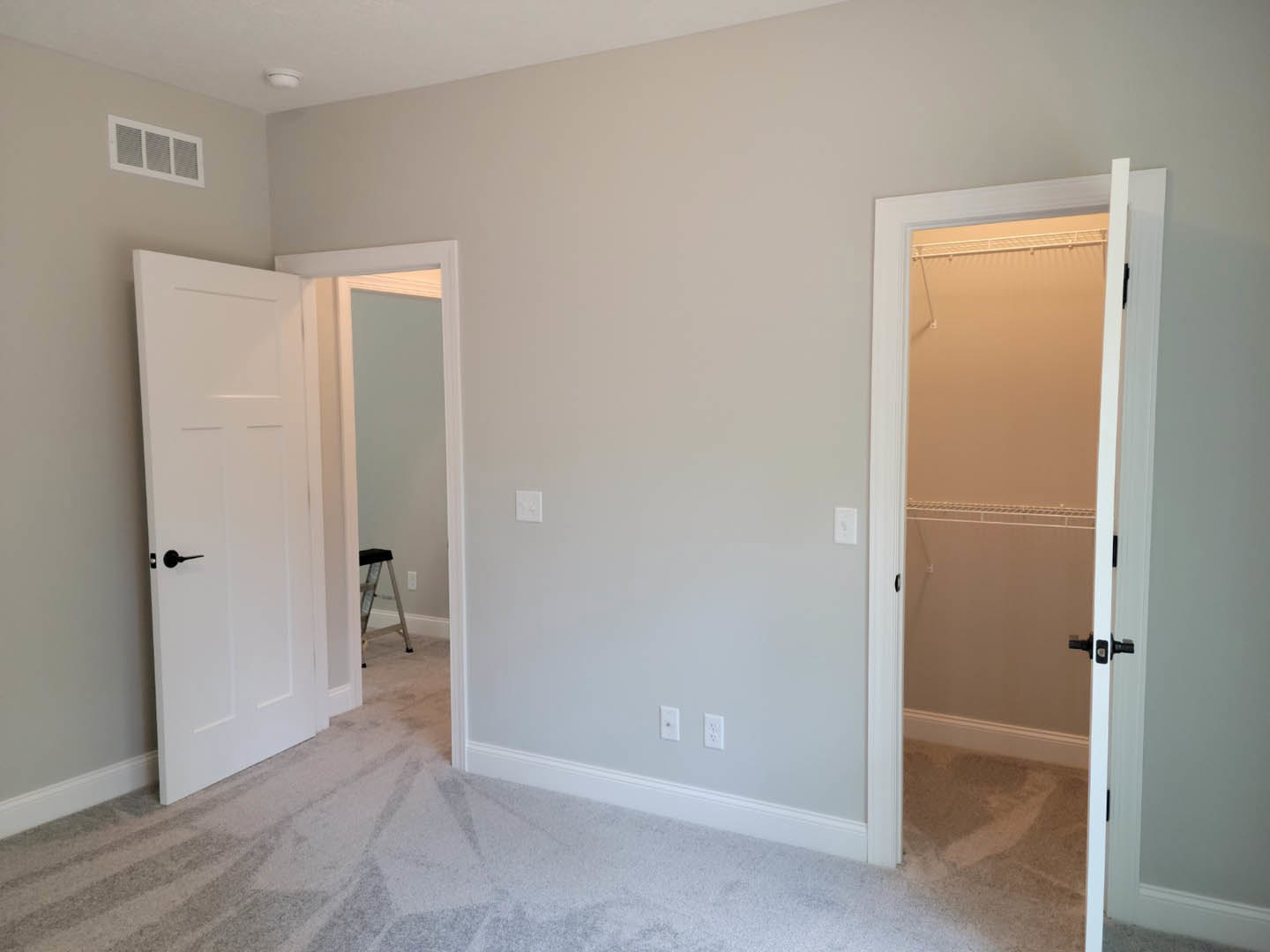 White walls, white closet door with black handle, ladder leaning against wall, floor vent, white baseboard molding