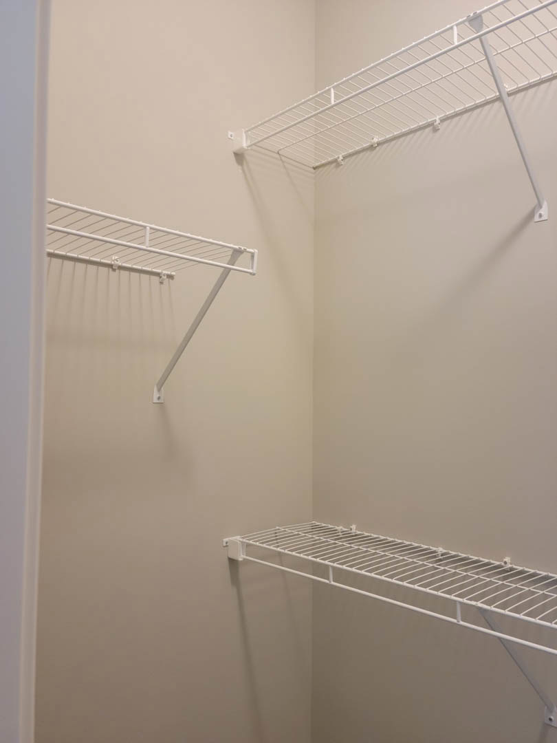 White wire shelving mounted on a closet wall with a metal rod for hanging clothes.