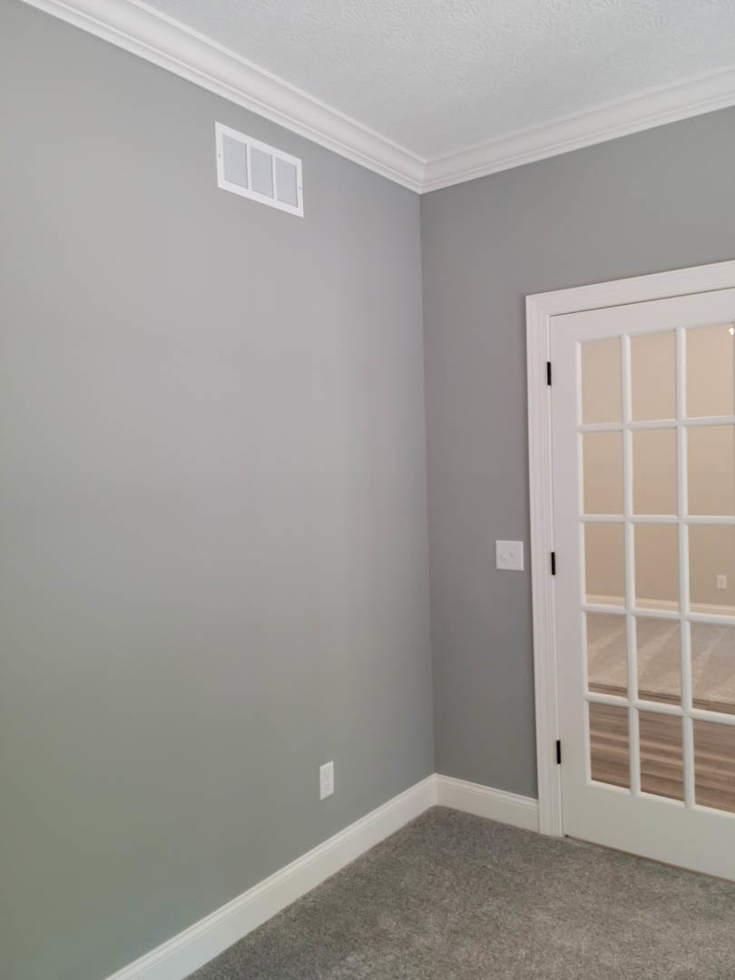Carpeted room featuring a white paneled door, adjacent glass door, wall vent, and white ceiling with crown molding