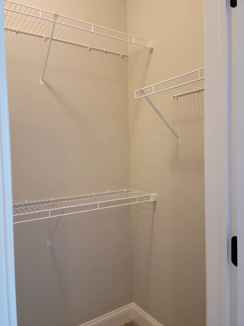 White wire shelving and metal hanging rod mounted on a white plaster closet wall with base molding