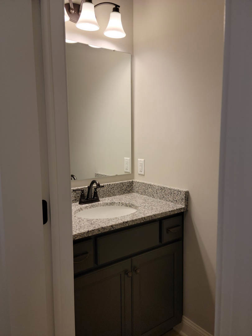 Modern bathroom featuring a rectangular mirror above a white countertop with a sleek chrome faucet, black cabinetry below, white tile walls with black trim, and a contemporary