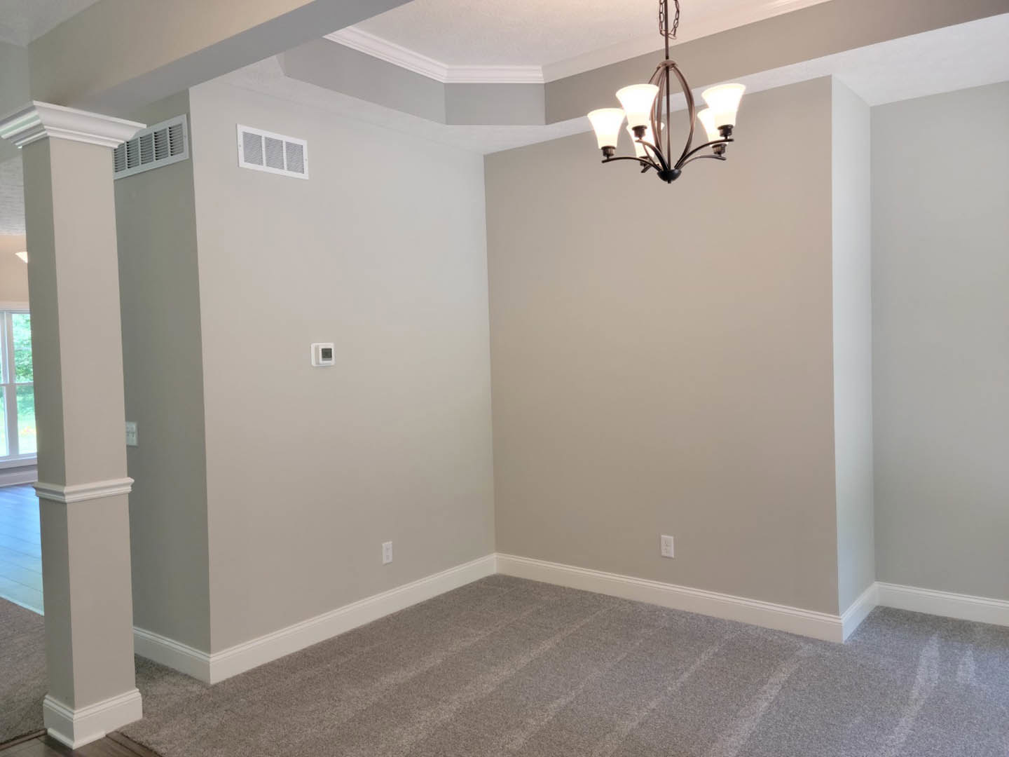 Carpeted living space with ornate chandelier, white pillar, wall vent, and decorative ceiling molding