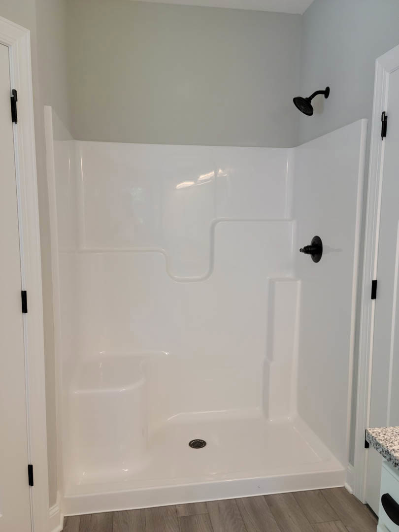 White tile shower with matte black shower head and handle, wood floor with white baseboard, plaster wall.