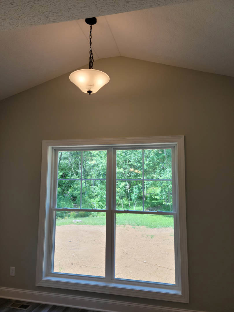 Pendant light with metal chain hanging from white ceiling near window with tree view, black fixture contrasts with bright interior.