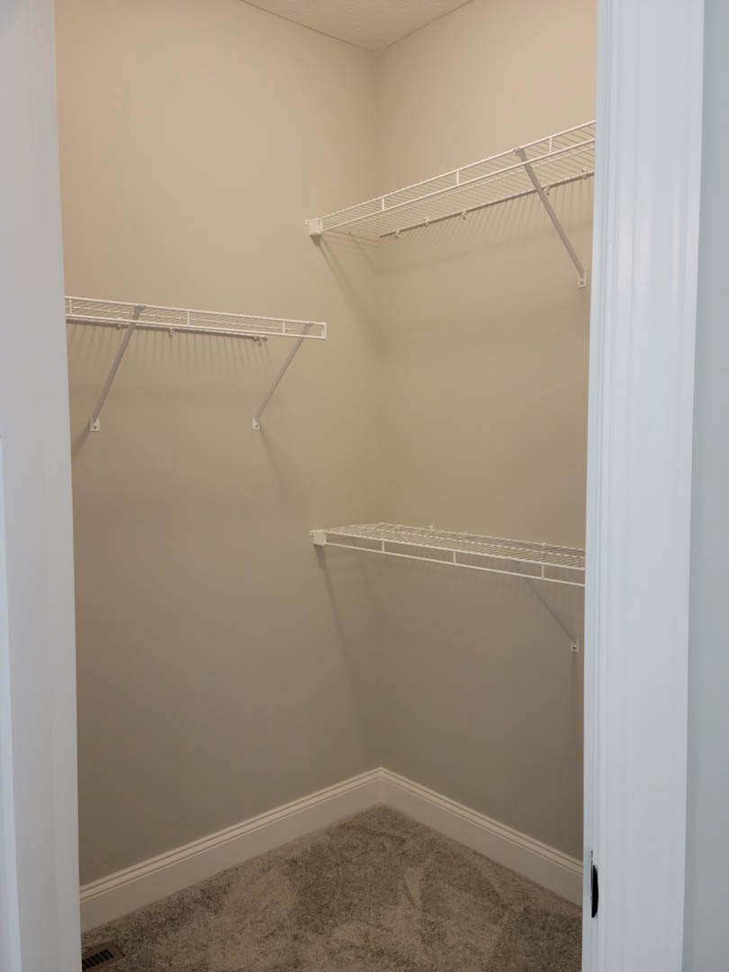 Walk-in closet with white shelves, clothes rack, metal wall grate, and plaster walls; close-up of dirty floor and white wall.