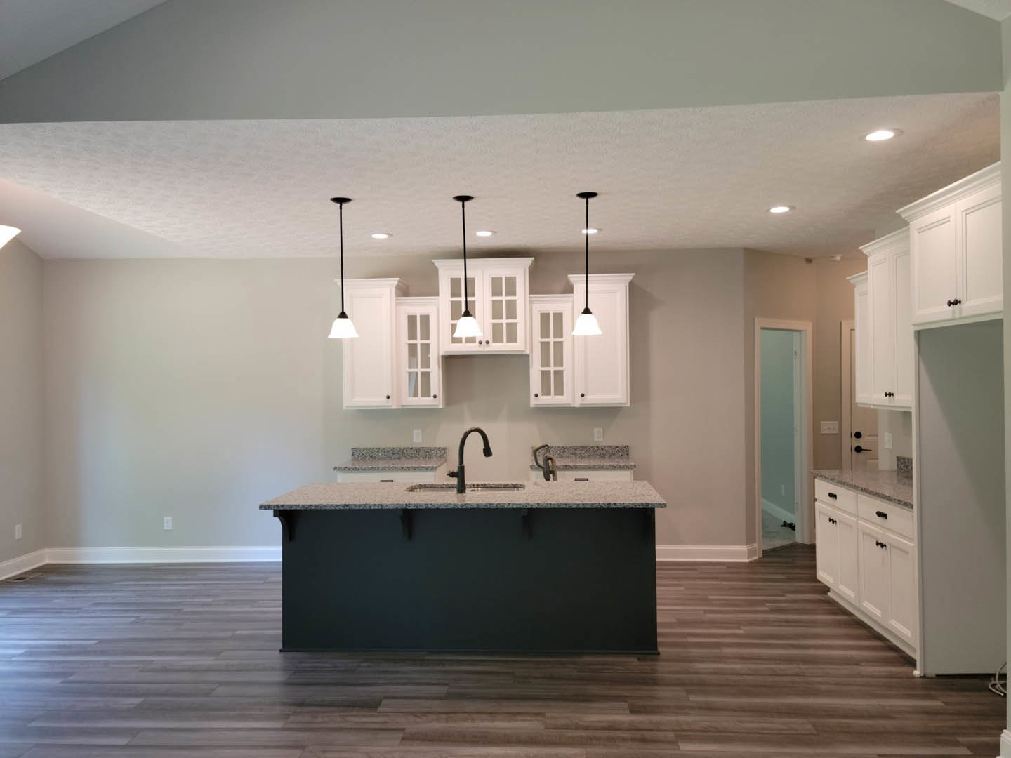 Spacious kitchen featuring a large central island with white quartz countertop, modern cabinetry, stainless steel sink, tile backsplash, and light wood flooring.