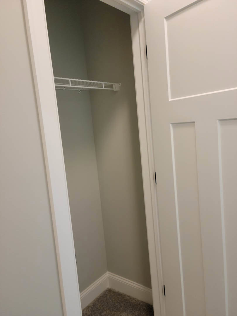 White closet door with brushed metal handle, smooth plaster walls, and built-in shelving visible inside.
