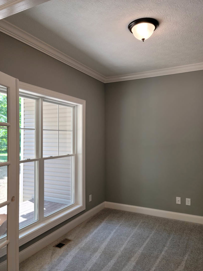 Neutral-toned room with carpet flooring, white framed window, ceiling-mounted light fixture, and white door with glass panels
