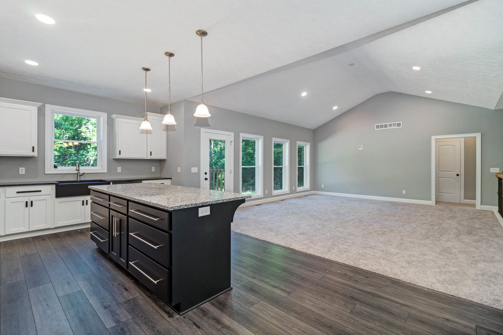Open concept kitchen and living room featuring a marble-topped island with drawers, window above sink and faucet, white door with black handle, carpeted floor, and detailed ceiling