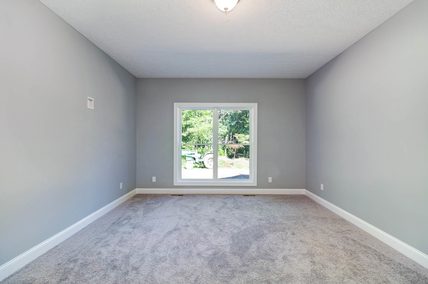Carpeted room with white ceiling and recessed light, large window overlooking grassy yard with green tractor.