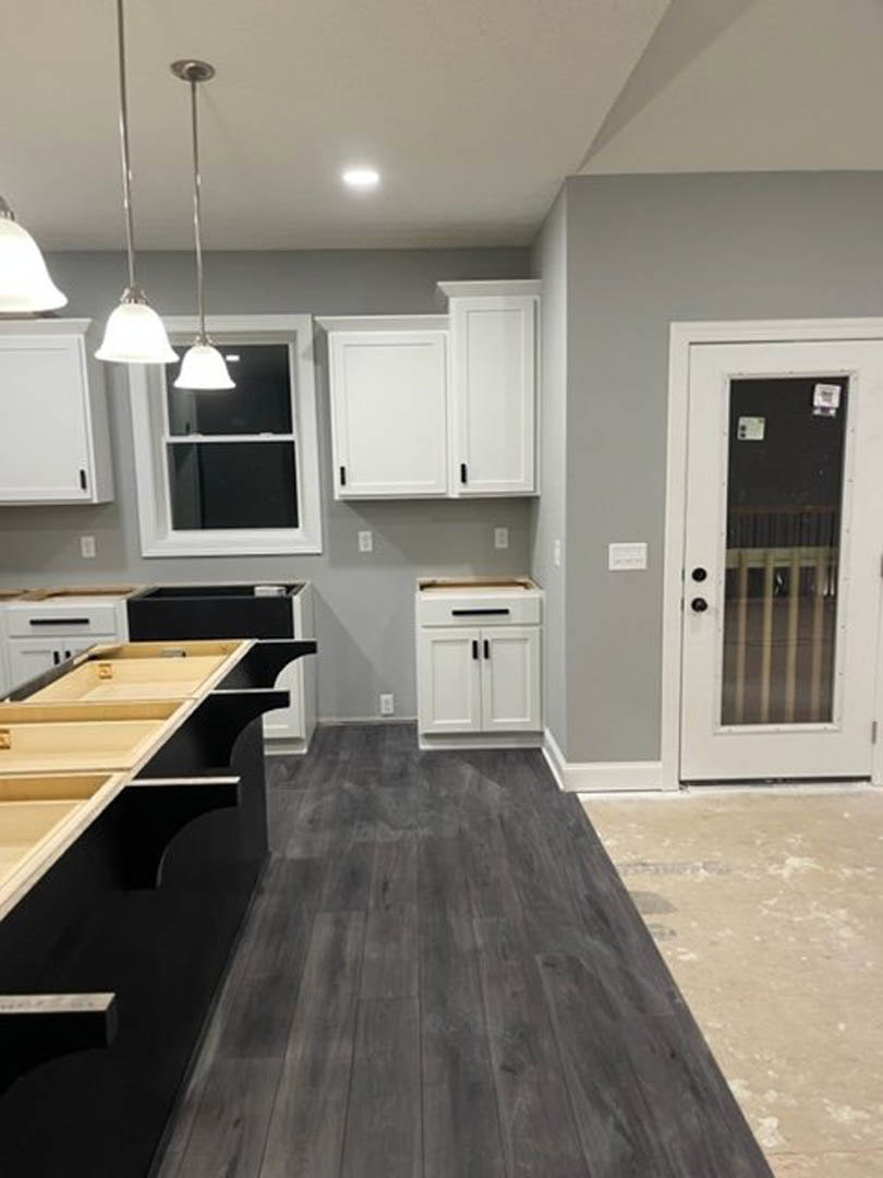 White kitchen cabinets with black countertops, dark wood flooring, black cabinet handles, stainless steel sink, and modern appliances