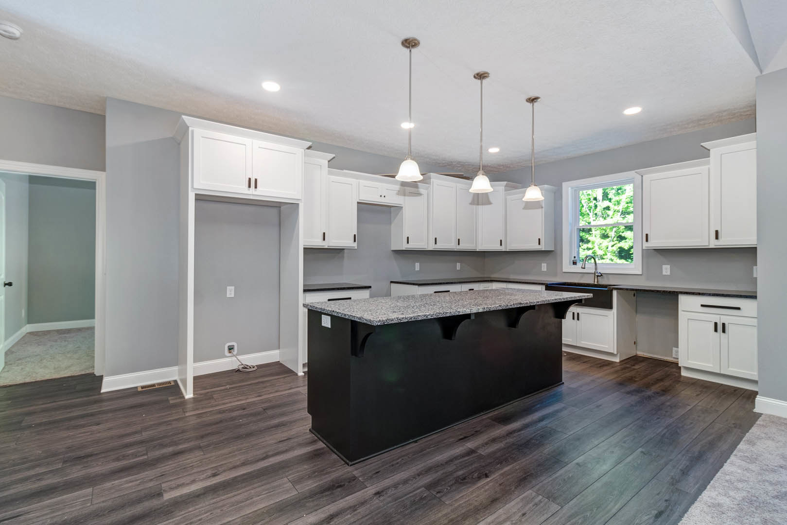 Kitchen featuring a black island with white cabinets, black and white countertops, wood flooring, large window overlooking trees, and modern pendant lighting