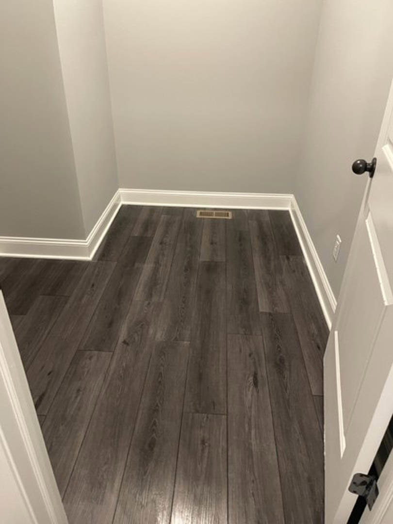 Hardwood floor with natural grain, white plaster walls, white paneled door with silver knob, ceiling finished in smooth white paint
