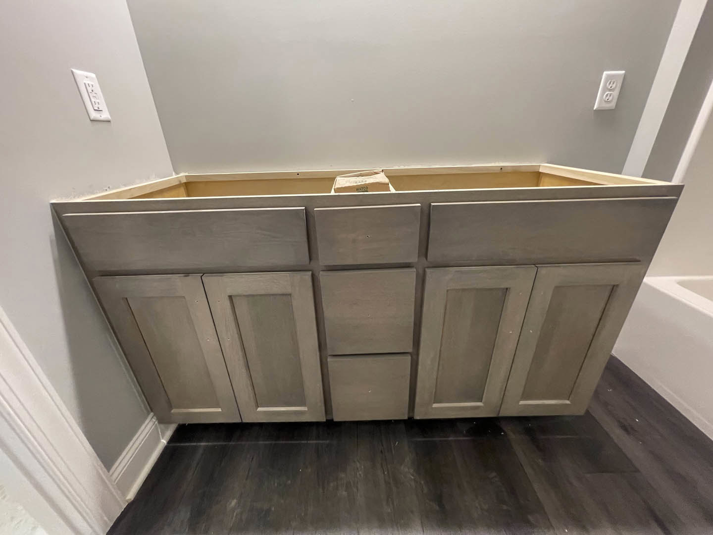 White shaker kitchen cabinets with brushed nickel hardware, dark wood flooring, quartz countertop, and a wall outlet visible near the backsplash