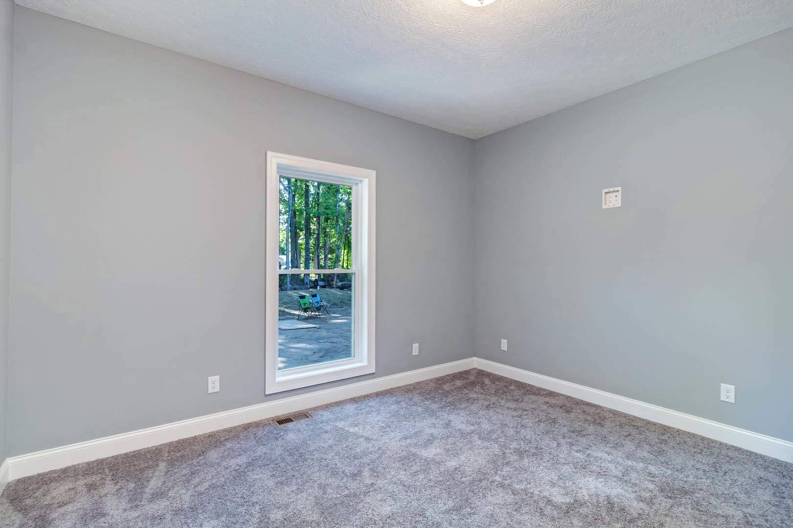 Bright room with white walls, white ceiling, large window overlooking blue and green lawn chairs, carpeted floor