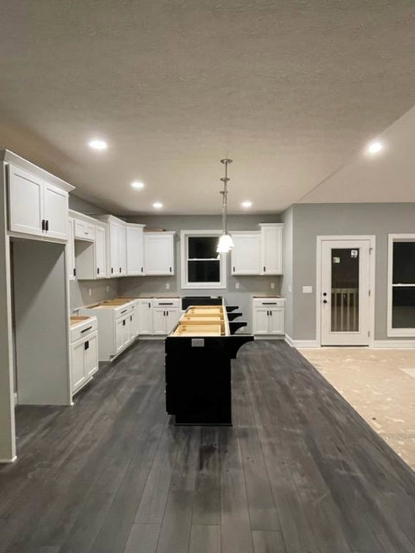 Kitchen with white shaker cabinets, black island with waterfall countertop, stainless steel sink, light wood laminate flooring, recessed lighting, white window frame, and modern