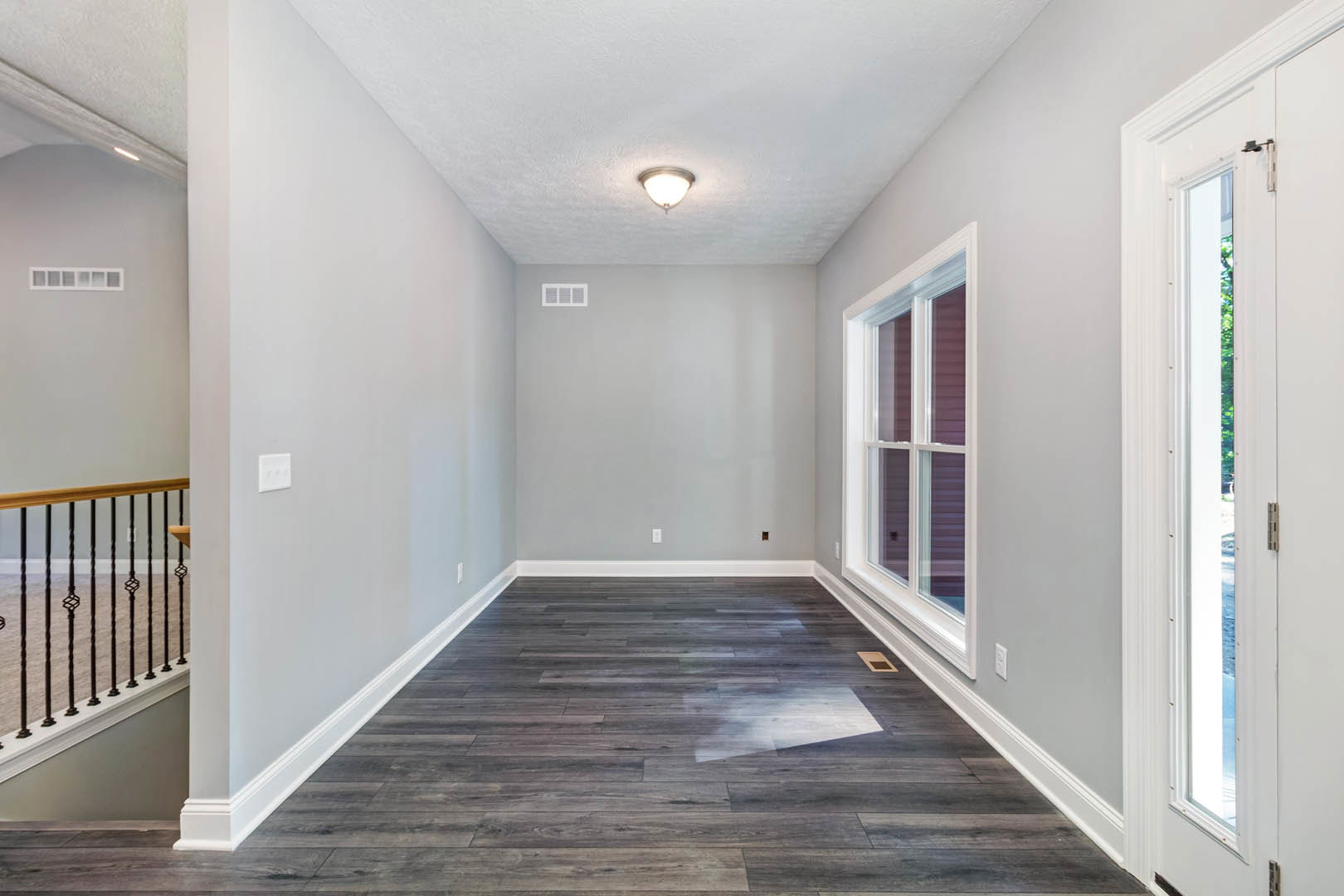 Hardwood floor with white walls, large window, modern ceiling light fixture, close-up of wood railing and light switch