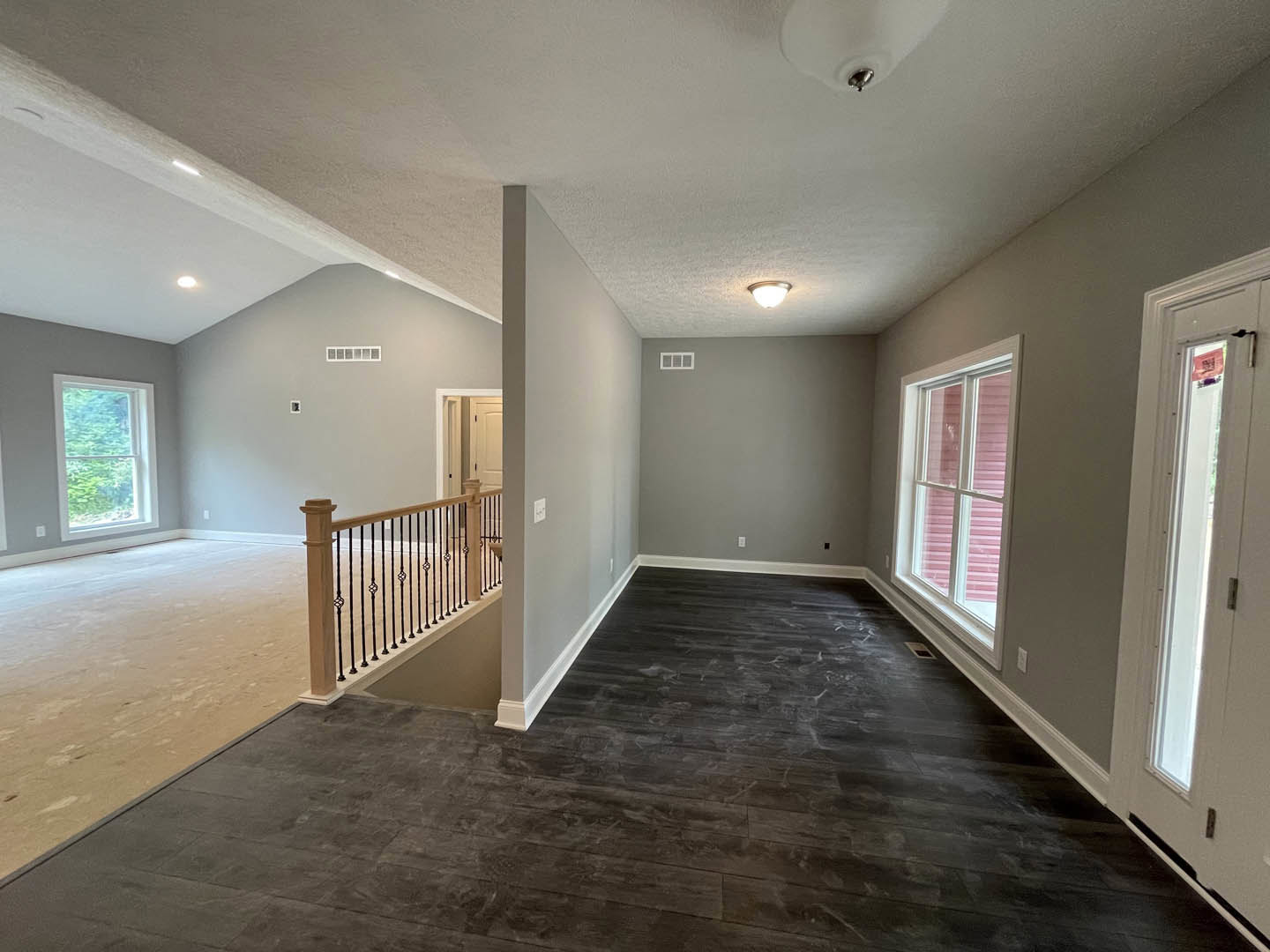 Dark wood flooring in a room featuring a staircase with a close-up of the railing, a window with pink blinds overlooking trees, and a white door with a window.