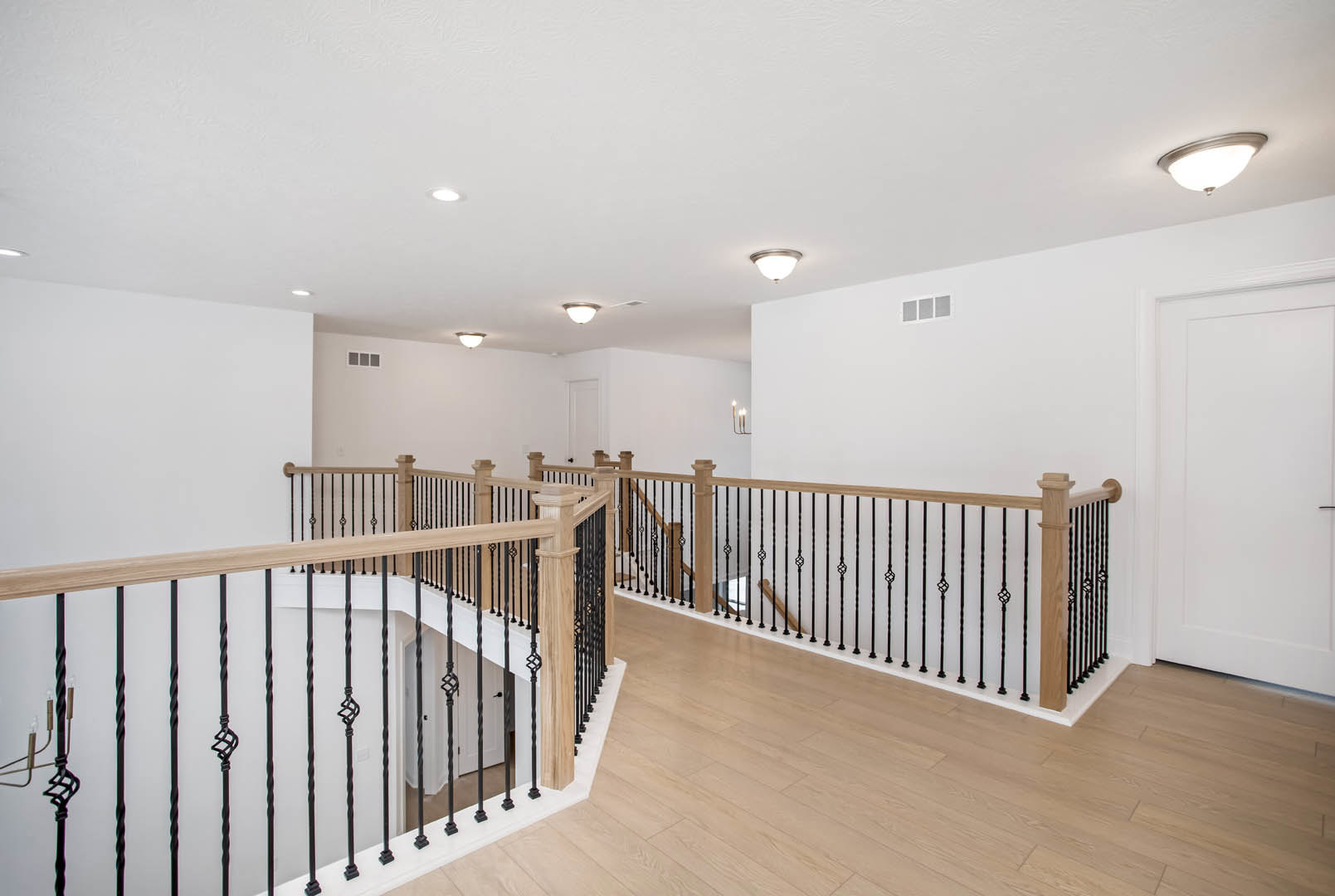 Open staircase with metal railings, white walls, light wood flooring, white door with black handle, recessed ceiling lights