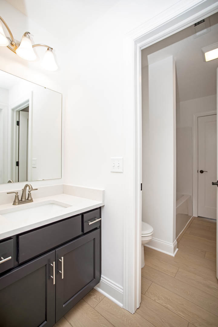 Modern bathroom featuring a rectangular sink with chrome faucet, large frameless mirror above tiled backsplash, white cabinetry, and a white door with brushed metal handle