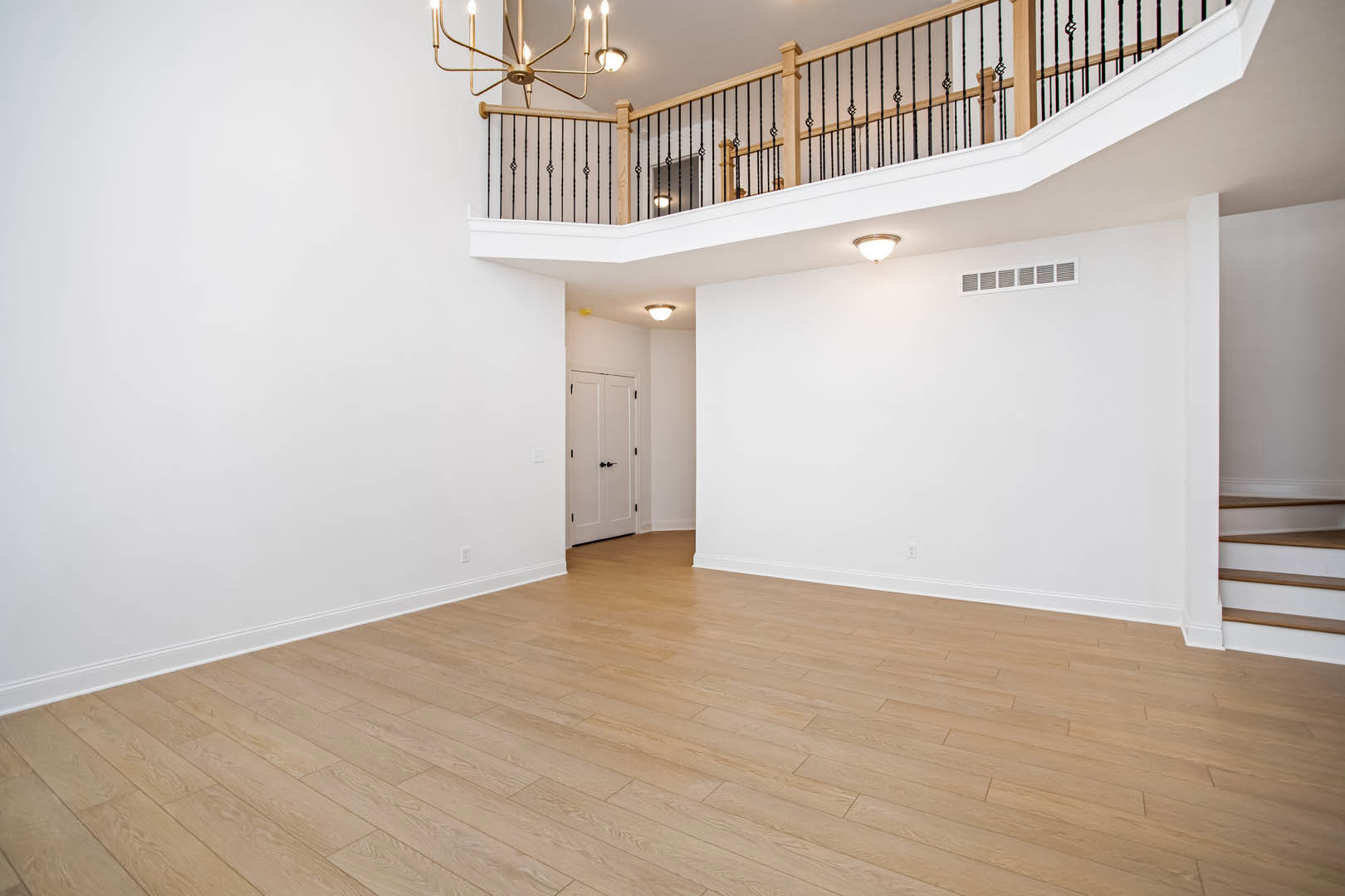 Hardwood floor room with three-light chandelier, white door with black handles, staircase with wood handrail, and plaster walls