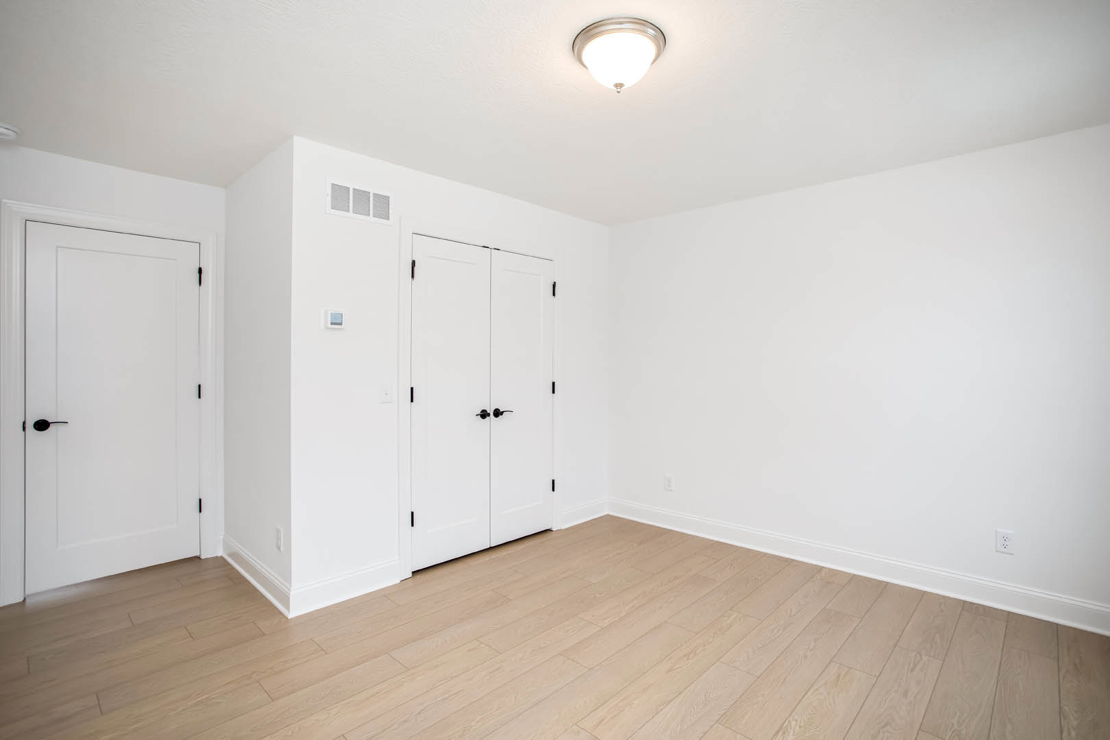 White walls and doors with black handles, wood flooring, ceiling light fixture