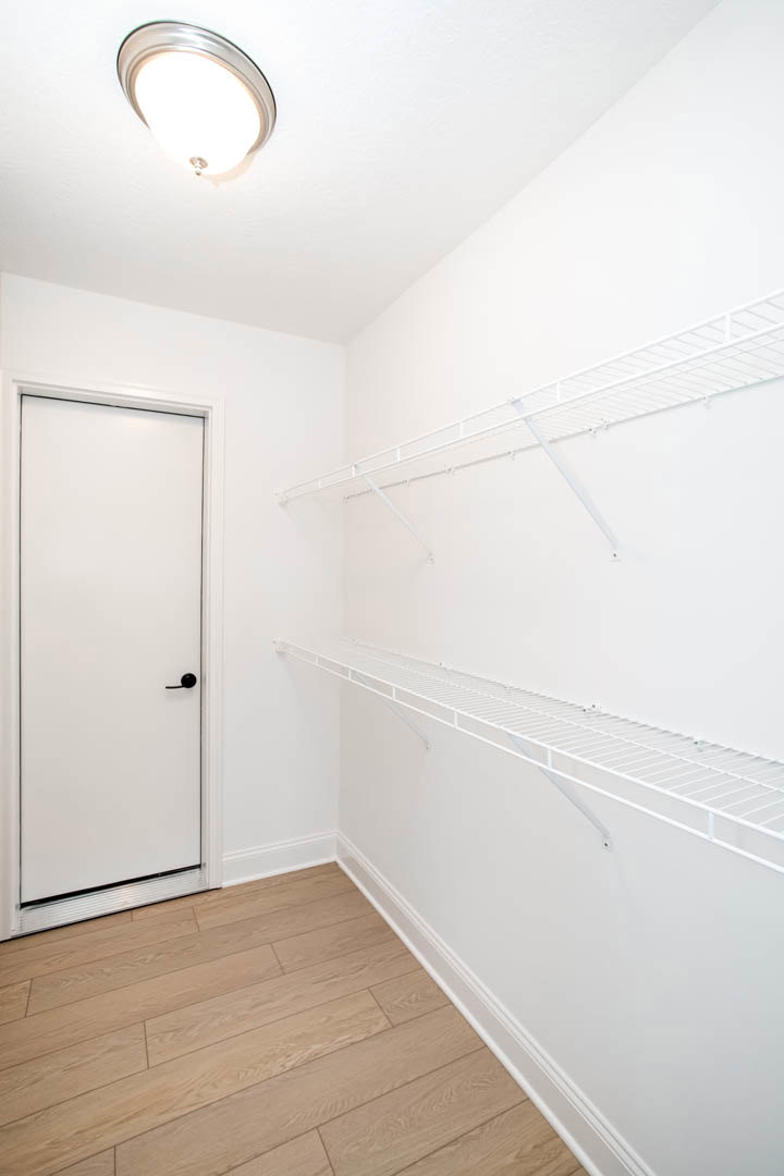 White closet with built-in shelves, white door featuring a black handle, wood flooring, white walls, ceiling light fixture