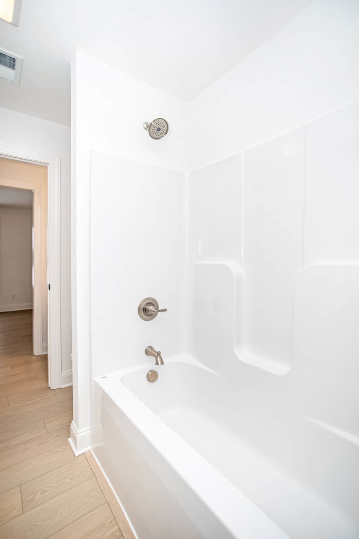 Freestanding white bathtub with silver faucet against white plaster wall with black border, marble tile floor visible