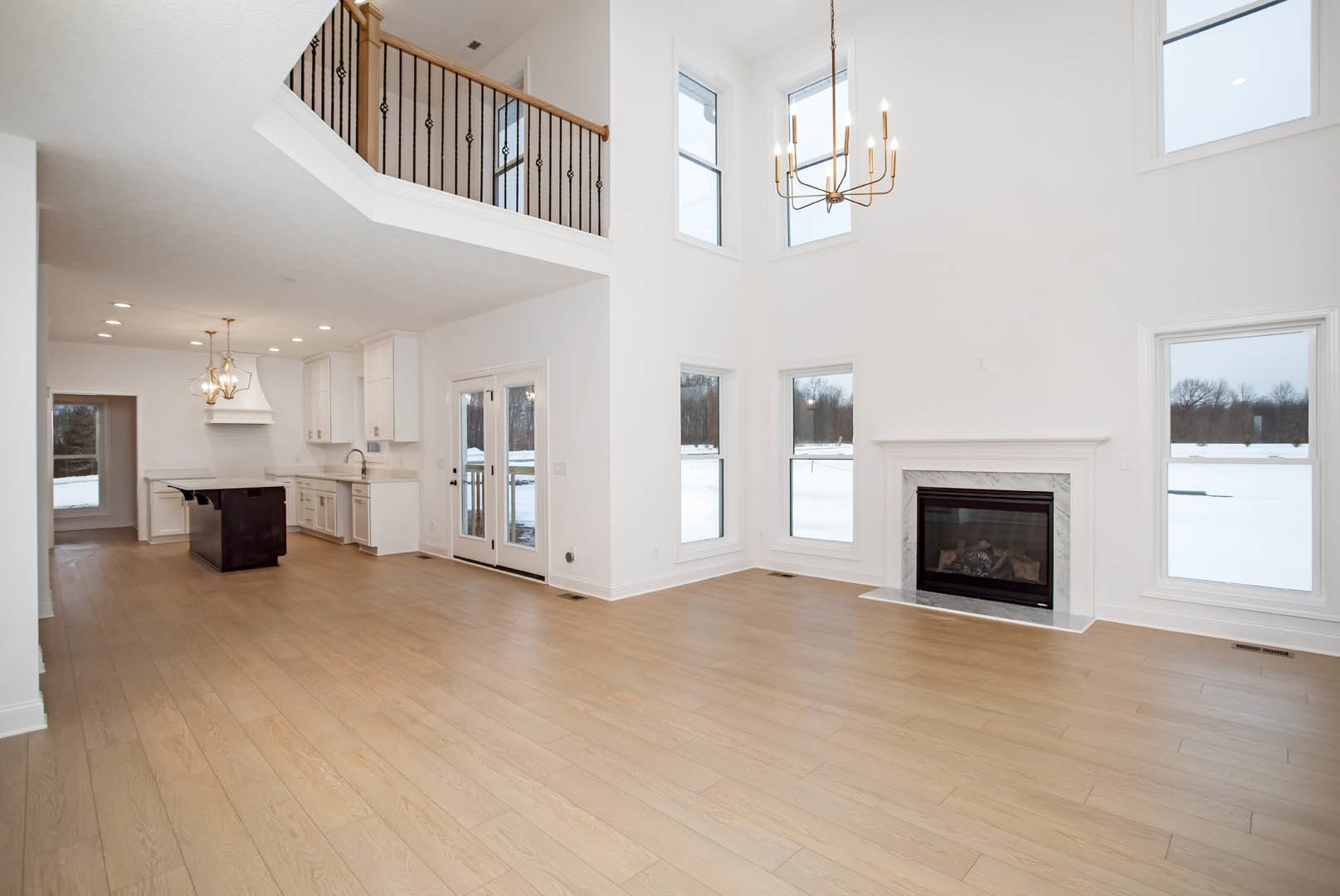 Living room with hardwood floors, modern fireplace with glass door, large windows overlooking snowy landscape, white walls, and built-in cabinetry.