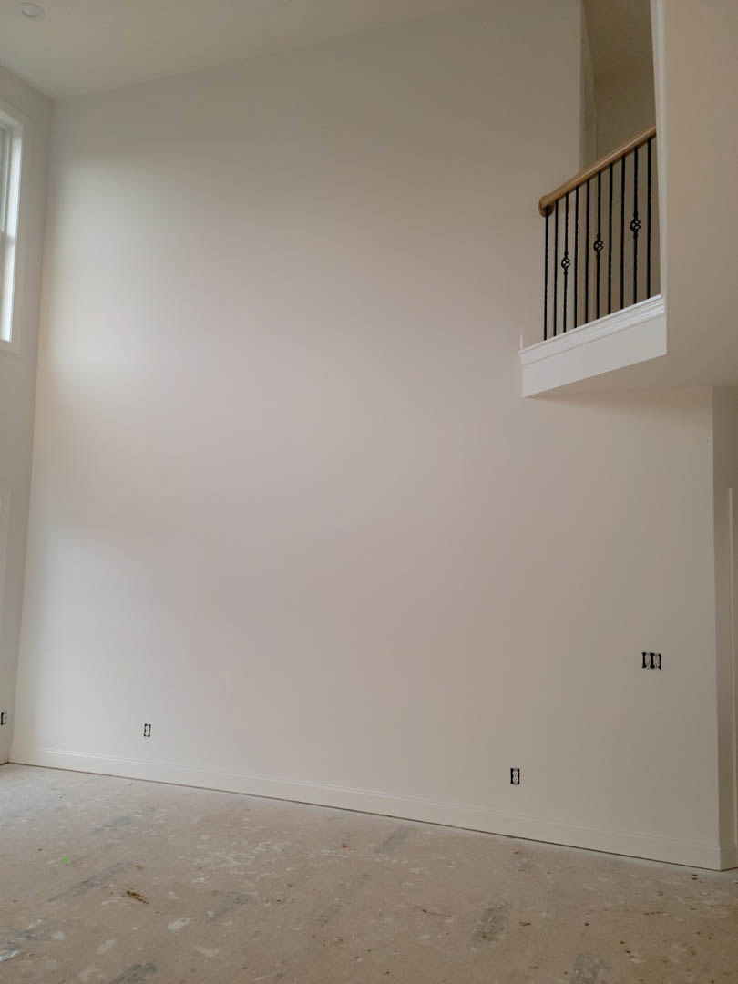 Open living area featuring a wooden staircase with black metal railing, white plaster walls, light hardwood flooring, and a balcony overlooking the space.