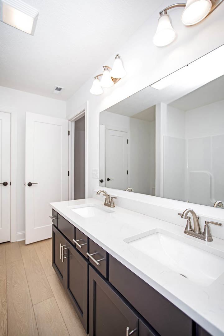 Bathroom with double vanity featuring white sinks, wide mirror above, wood flooring, white cabinetry, and ceiling light fixture