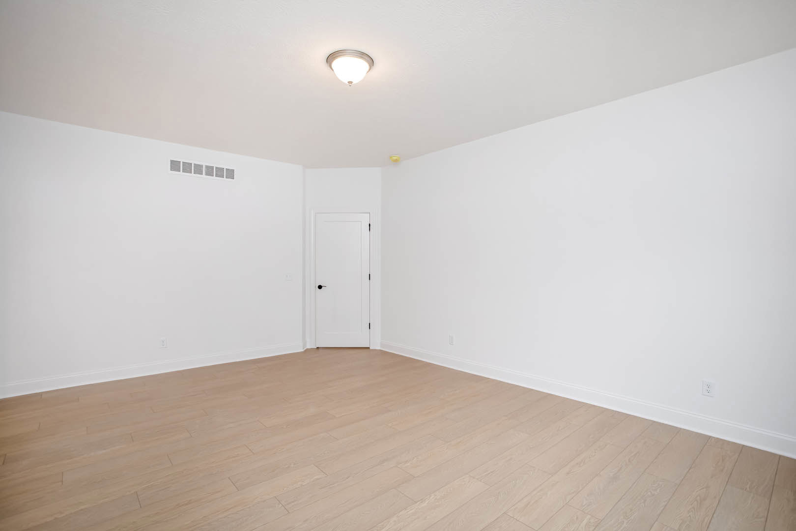 White walls and ceiling, open white door with black handle, light fixture overhead, hardwood floor throughout the room