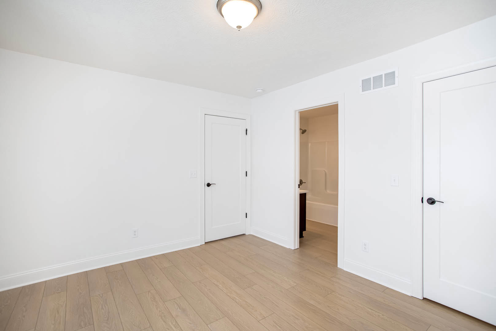 White paneled door with black handle opening into a room with light wood flooring and smooth white walls