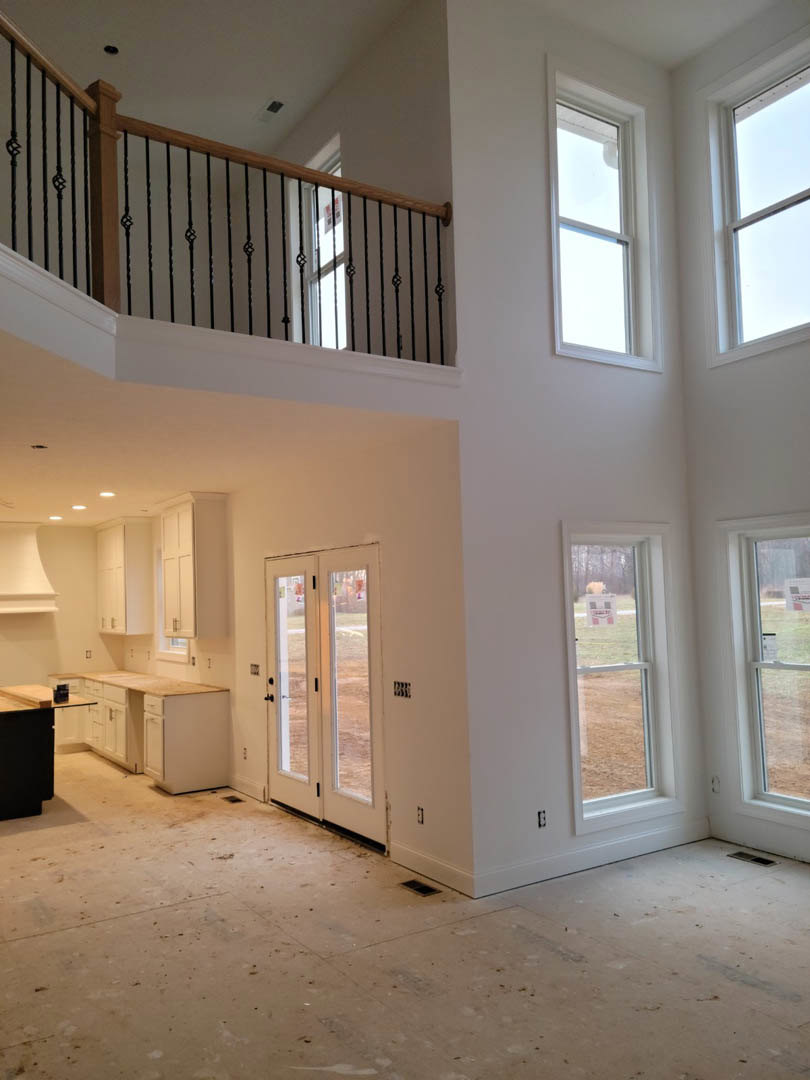 Open living area featuring a wooden staircase with white risers, large second story window with white trim, light plaster walls, hardwood flooring, and a paneled door.