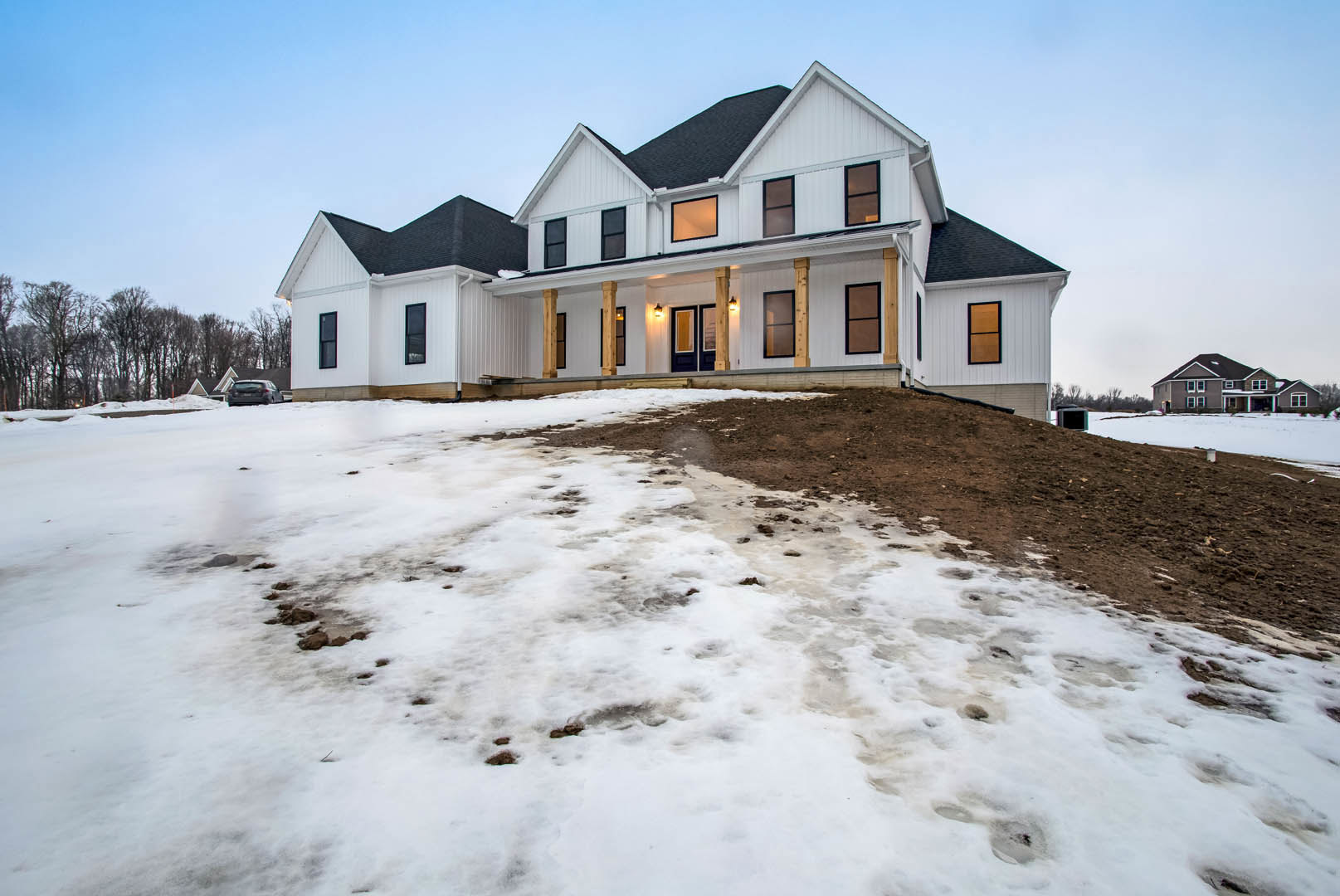 Large white house with black roof and window frames, surrounded by snow-covered ground and bare trees under a winter sky