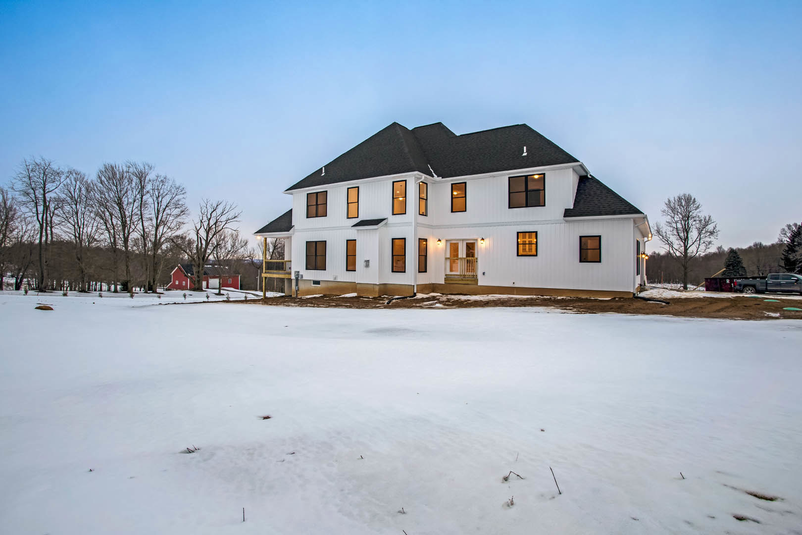 Large white two-story house with black roof, surrounded by snow-covered ground and leafless trees, winter sky overhead.