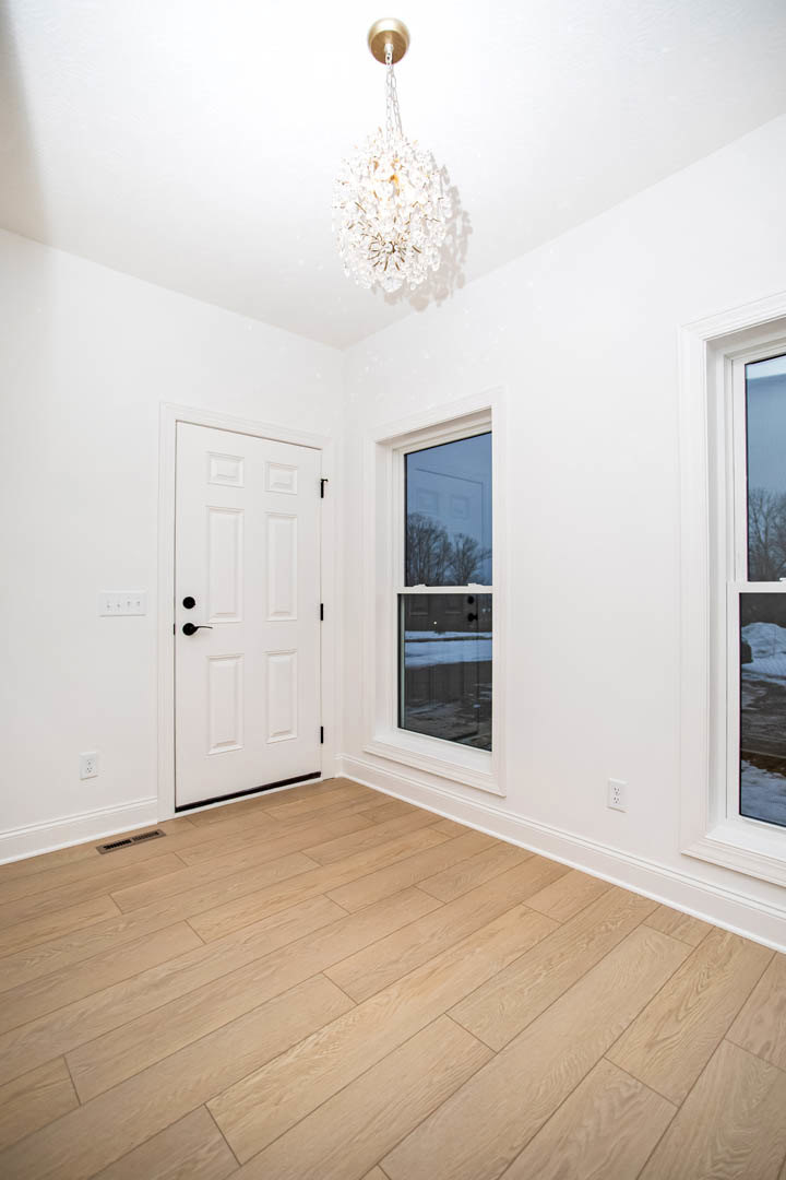 White paneled door with black handles, wood flooring, large windows overlooking snowy forest, modern chandelier, white walls with crown molding